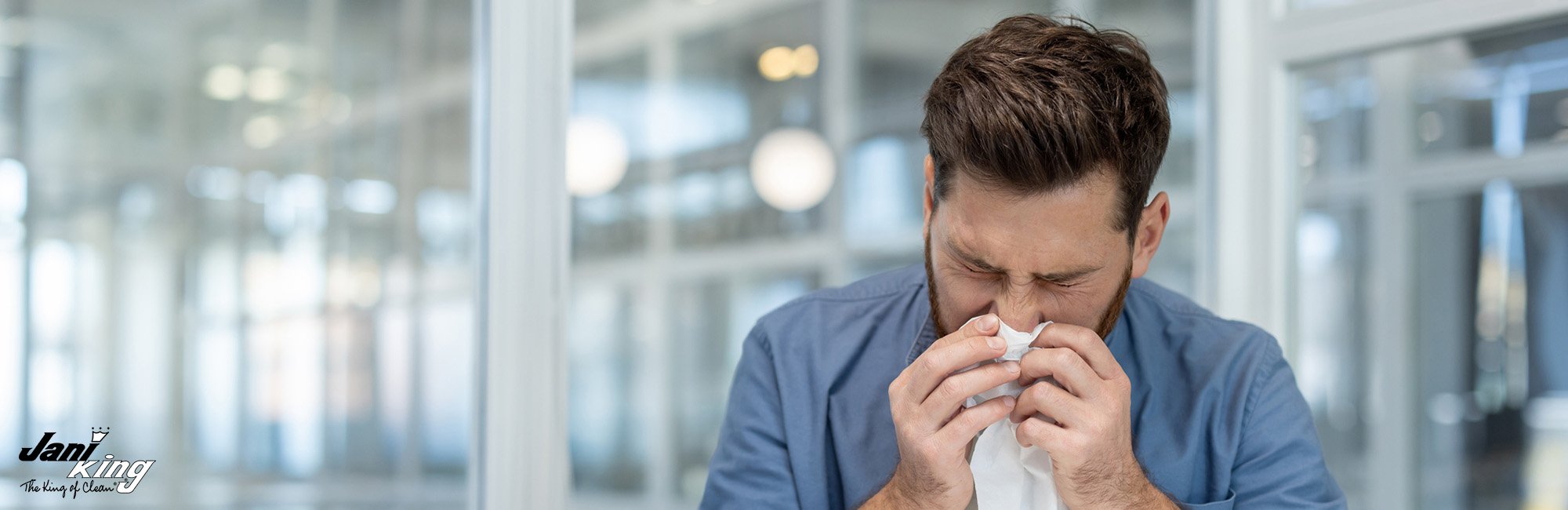 Man in a business building blowing his nose, indicating that he is coming down with a cold.
